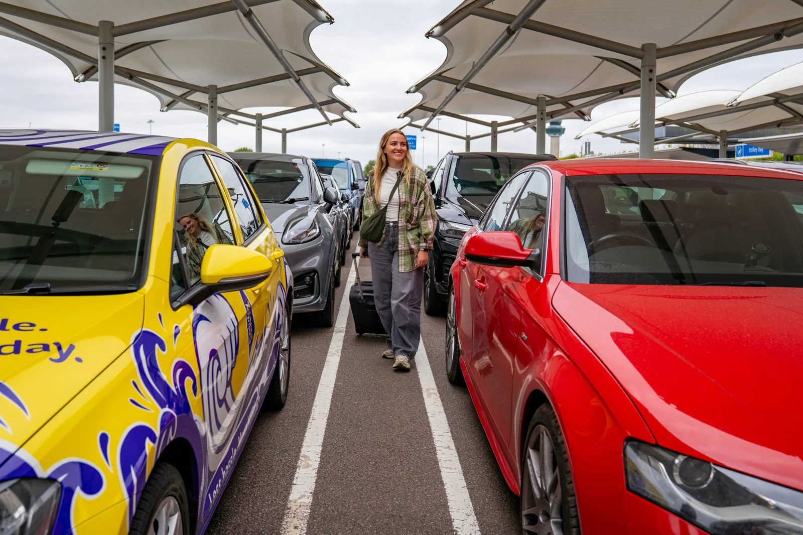 Traveller with suitcase between parked cars at Stansted Airport